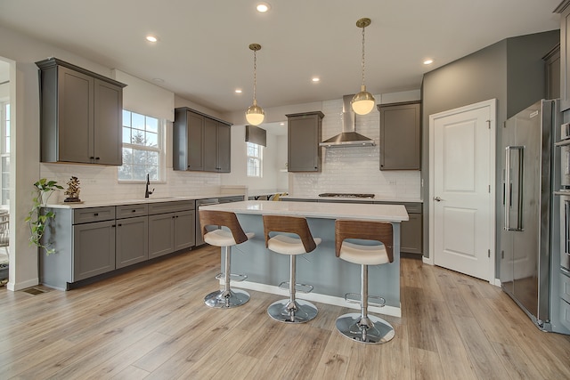 kitchen with high end refrigerator, wall chimney exhaust hood, a kitchen island, light wood-type flooring, and a sink