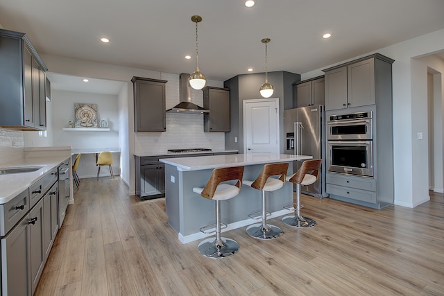 kitchen featuring a breakfast bar area, appliances with stainless steel finishes, a kitchen island, light wood-type flooring, and wall chimney exhaust hood