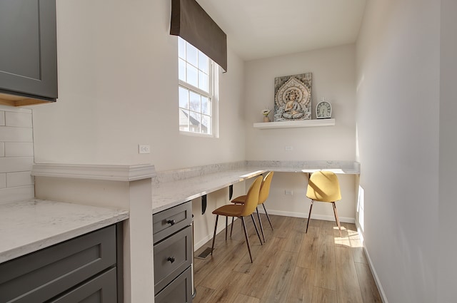 office area featuring light wood-type flooring, built in study area, and baseboards