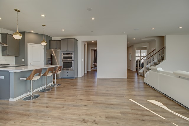 kitchen featuring open floor plan, stainless steel appliances, gray cabinets, light countertops, and a kitchen bar