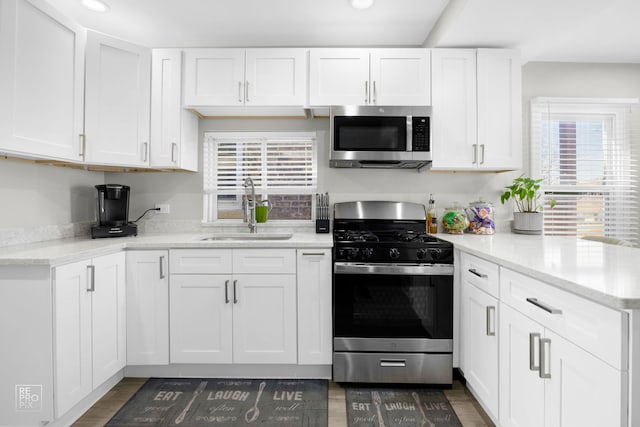 kitchen featuring stainless steel appliances, a peninsula, dark wood-style flooring, a sink, and white cabinetry