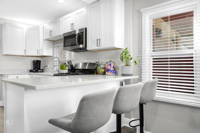 kitchen featuring range with gas stovetop, white cabinets, stainless steel microwave, and a kitchen bar