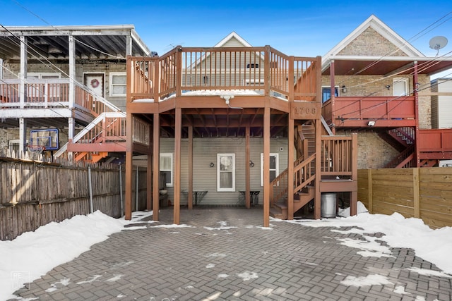 snow covered back of property featuring a deck, a patio area, a fenced backyard, and stairway