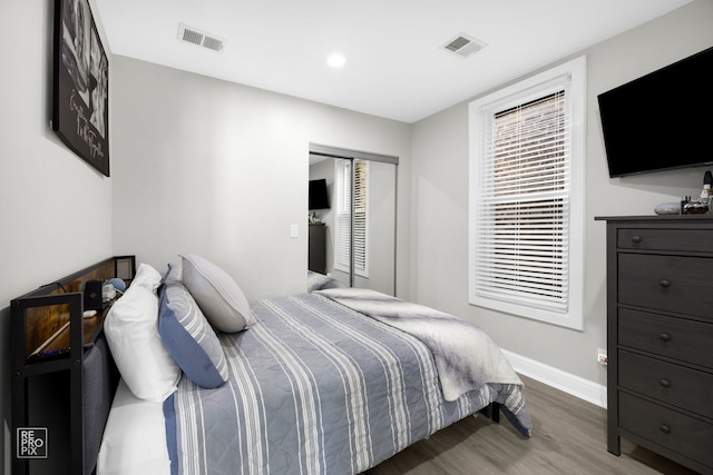 bedroom with a closet, wood finished floors, visible vents, and baseboards