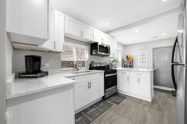 kitchen with white cabinets, appliances with stainless steel finishes, a peninsula, light wood-style floors, and a sink