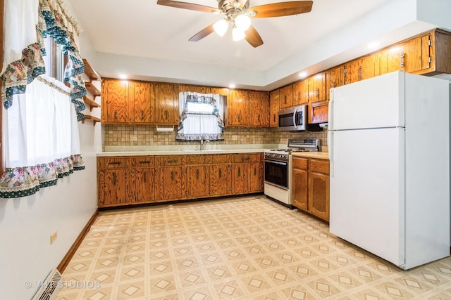 kitchen featuring freestanding refrigerator, a sink, gas range, stainless steel microwave, and brown cabinets