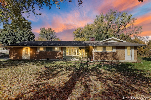 ranch-style home with brick siding, a chimney, and a front lawn