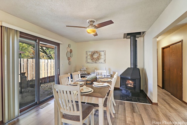 dining space featuring a textured ceiling, wood finished floors, a ceiling fan, baseboards, and a wood stove