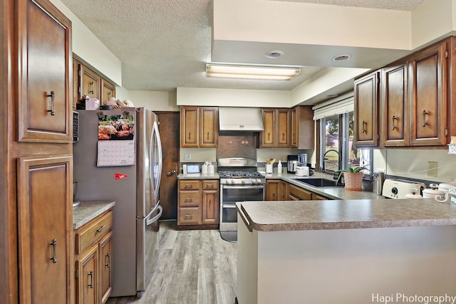 kitchen with light wood-style flooring, stainless steel appliances, premium range hood, a peninsula, and a sink