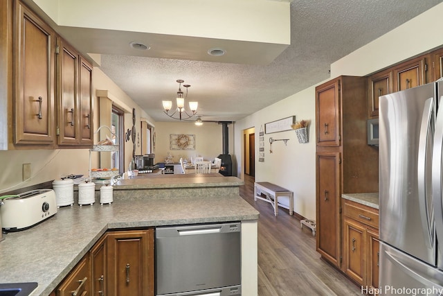 kitchen with a textured ceiling, a notable chandelier, a peninsula, wood finished floors, and appliances with stainless steel finishes