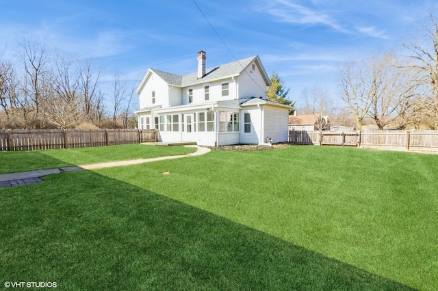 back of house featuring a yard, a chimney, a fenced backyard, and a sunroom