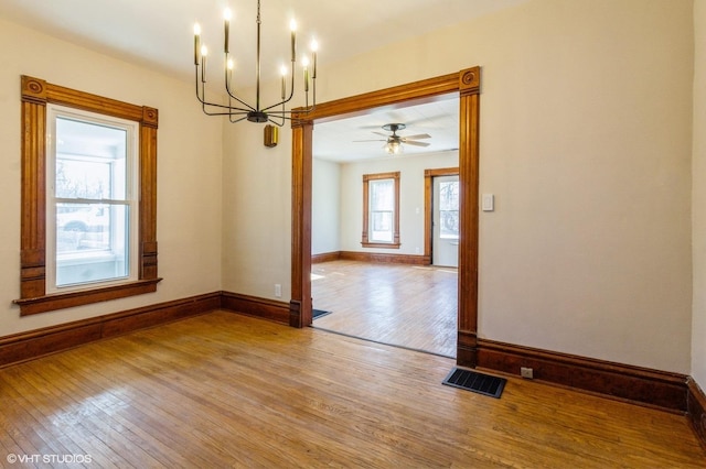 empty room featuring baseboards, ceiling fan with notable chandelier, visible vents, and light wood-style floors