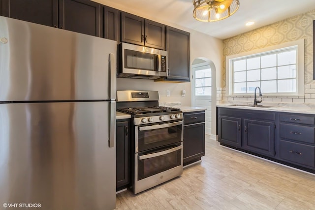 kitchen with arched walkways, a sink, stainless steel appliances, light countertops, and backsplash