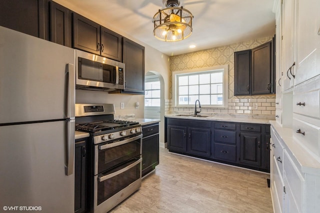 kitchen featuring arched walkways, stainless steel appliances, a sink, light countertops, and wallpapered walls