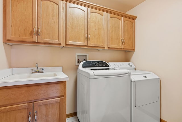 clothes washing area with baseboards, a sink, cabinet space, and washer and dryer