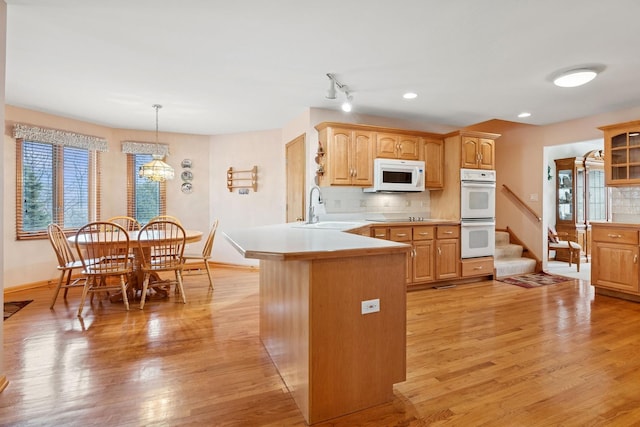 kitchen with a peninsula, white appliances, light wood finished floors, and a sink