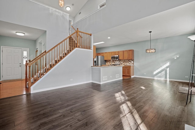 unfurnished living room featuring visible vents, a towering ceiling, stairs, baseboards, and dark wood-style floors