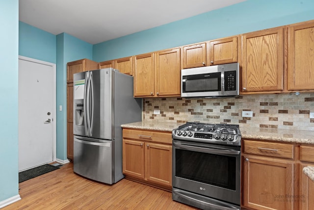 kitchen featuring baseboards, appliances with stainless steel finishes, light wood-type flooring, light stone countertops, and tasteful backsplash