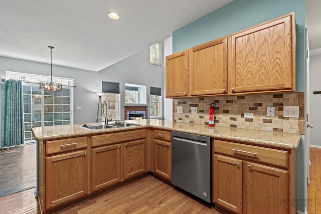 kitchen featuring light wood finished floors, decorative backsplash, a sink, dishwasher, and a peninsula