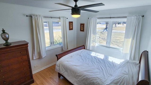 bedroom with light wood-style floors, ceiling fan, multiple windows, and baseboards