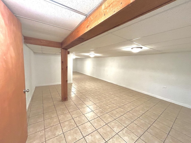 finished below grade area with light tile patterned floors, a paneled ceiling, and baseboards