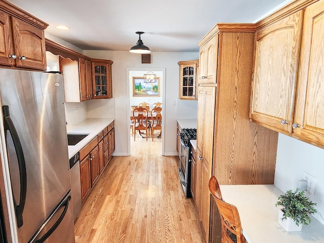 kitchen with appliances with stainless steel finishes, light wood-type flooring, visible vents, and glass insert cabinets