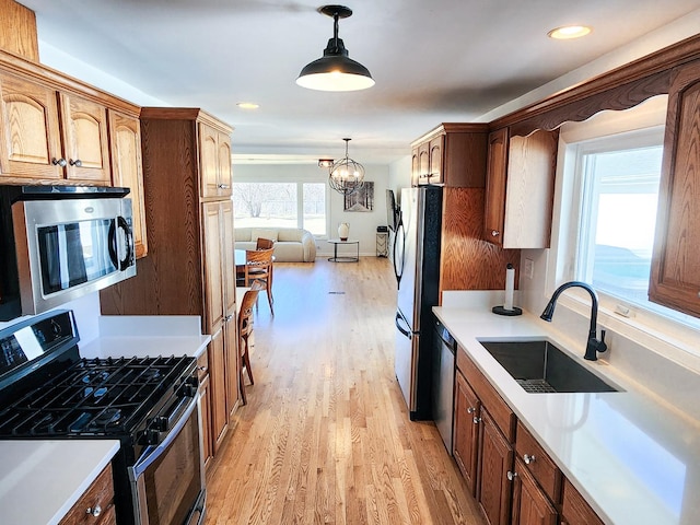 kitchen with decorative light fixtures, light countertops, stainless steel appliances, light wood-style floors, and a sink