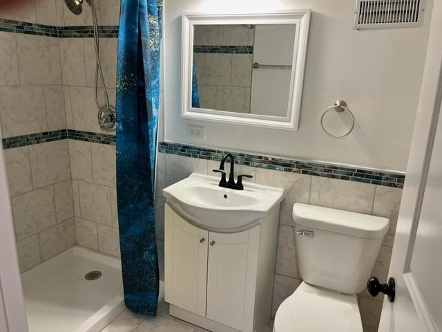 bathroom with toilet, a stall shower, visible vents, and vanity