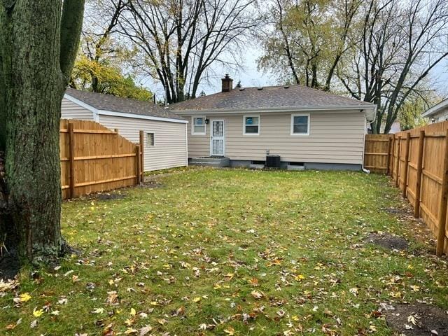 back of house with central air condition unit, a fenced backyard, a chimney, and a lawn