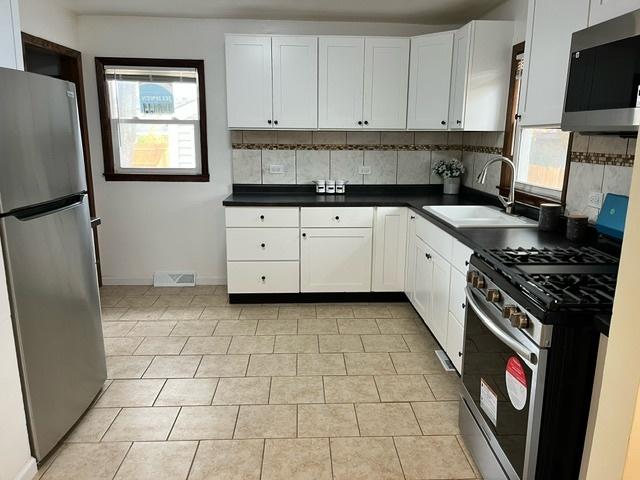 kitchen featuring a sink, appliances with stainless steel finishes, decorative backsplash, dark countertops, and plenty of natural light