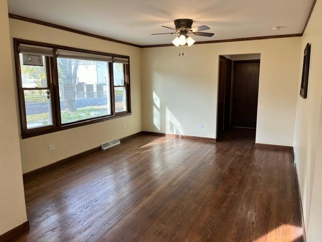 unfurnished room featuring dark wood finished floors, crown molding, visible vents, ceiling fan, and baseboards