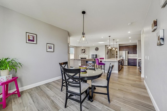 dining space featuring light wood-style flooring, a fireplace, and baseboards