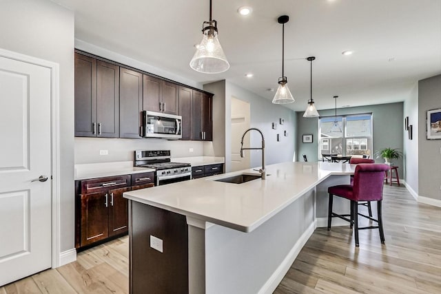 kitchen with light wood-style flooring, stainless steel appliances, a spacious island, a sink, and a kitchen breakfast bar