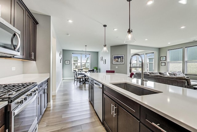 kitchen featuring recessed lighting, light countertops, appliances with stainless steel finishes, a sink, and dark brown cabinetry