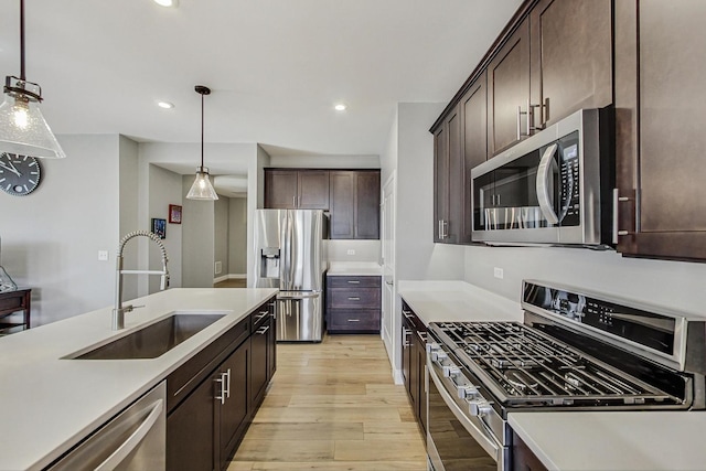 kitchen with light wood finished floors, appliances with stainless steel finishes, dark brown cabinets, pendant lighting, and a sink