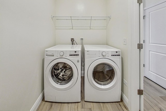 clothes washing area featuring laundry area, light wood finished floors, washing machine and clothes dryer, and baseboards