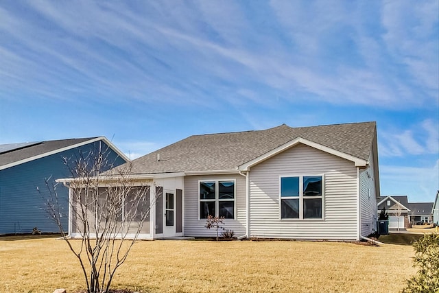 back of property with a garage, roof with shingles, and a yard