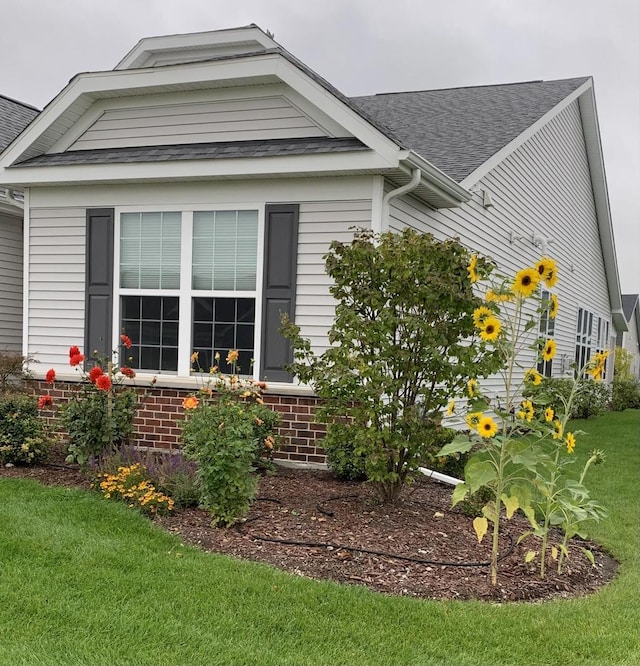 view of home's exterior with brick siding, a yard, and roof with shingles