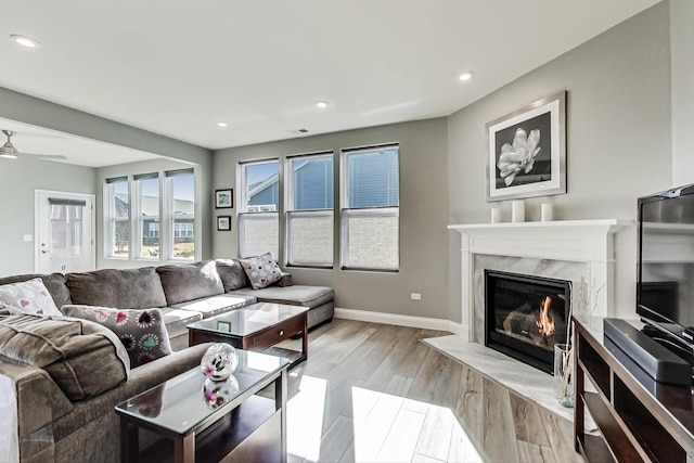 living area with recessed lighting, a premium fireplace, light wood-style floors, a ceiling fan, and baseboards