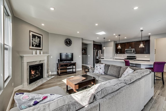 living room featuring baseboards, light wood finished floors, a high end fireplace, and recessed lighting