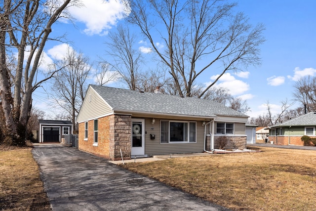 view of front of house featuring an outbuilding, roof with shingles, a front yard, stone siding, and driveway