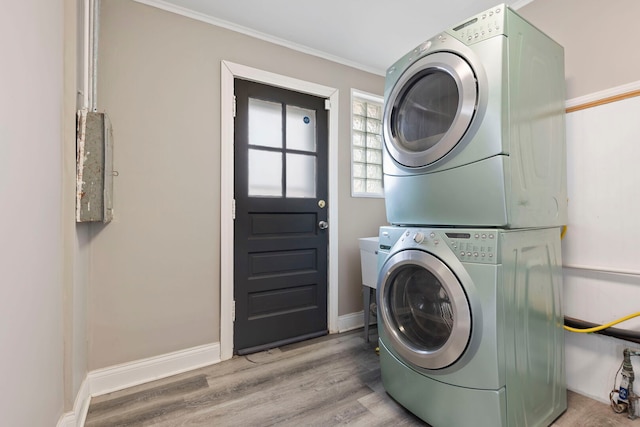 washroom featuring laundry area, baseboards, ornamental molding, stacked washer / drying machine, and wood finished floors