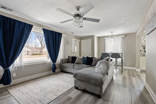 living room with a textured ceiling, wood finished floors, visible vents, and baseboards