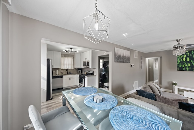 dining space featuring visible vents, baseboards, stacked washer / dryer, light wood-style flooring, and ceiling fan with notable chandelier