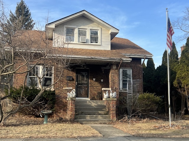 bungalow-style home featuring a shingled roof, cooling unit, covered porch, and brick siding