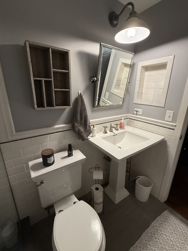 half bath featuring toilet, tile walls, a sink, and wainscoting