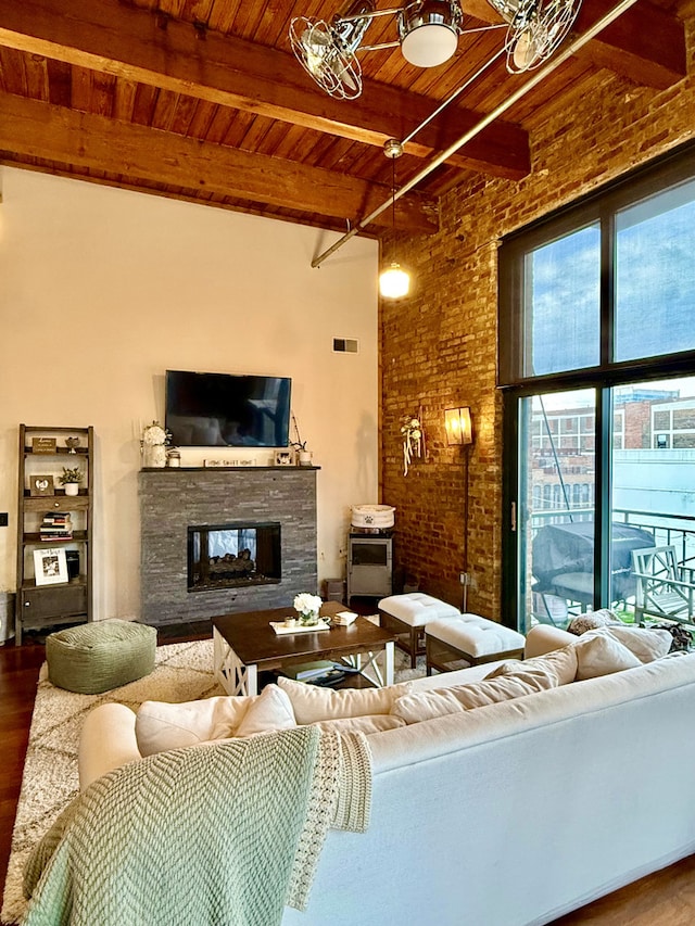 living area with a stone fireplace, beamed ceiling, wood finished floors, and wood ceiling