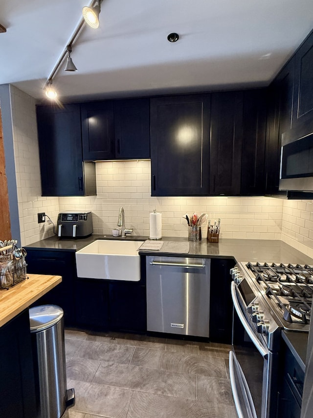 kitchen featuring dark cabinets, appliances with stainless steel finishes, backsplash, and a sink