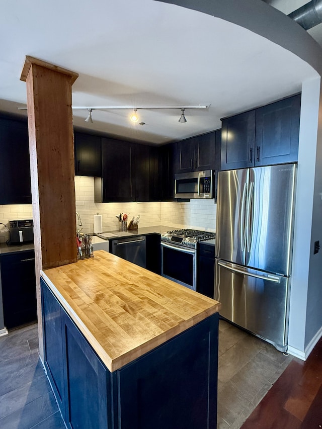 kitchen with appliances with stainless steel finishes, butcher block counters, a sink, and decorative backsplash