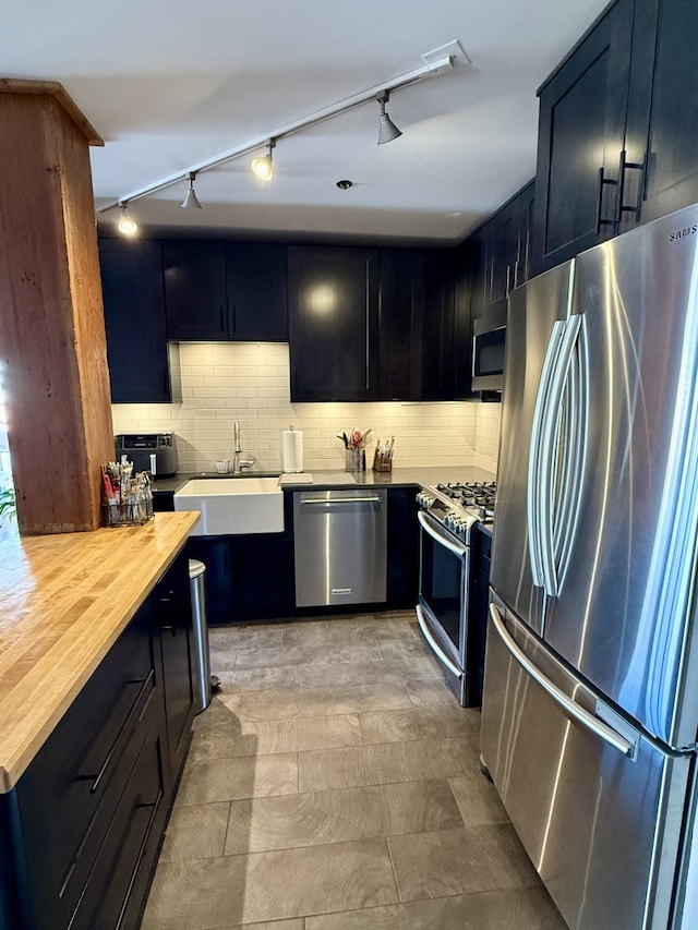 kitchen with stainless steel appliances, butcher block countertops, a sink, and decorative backsplash